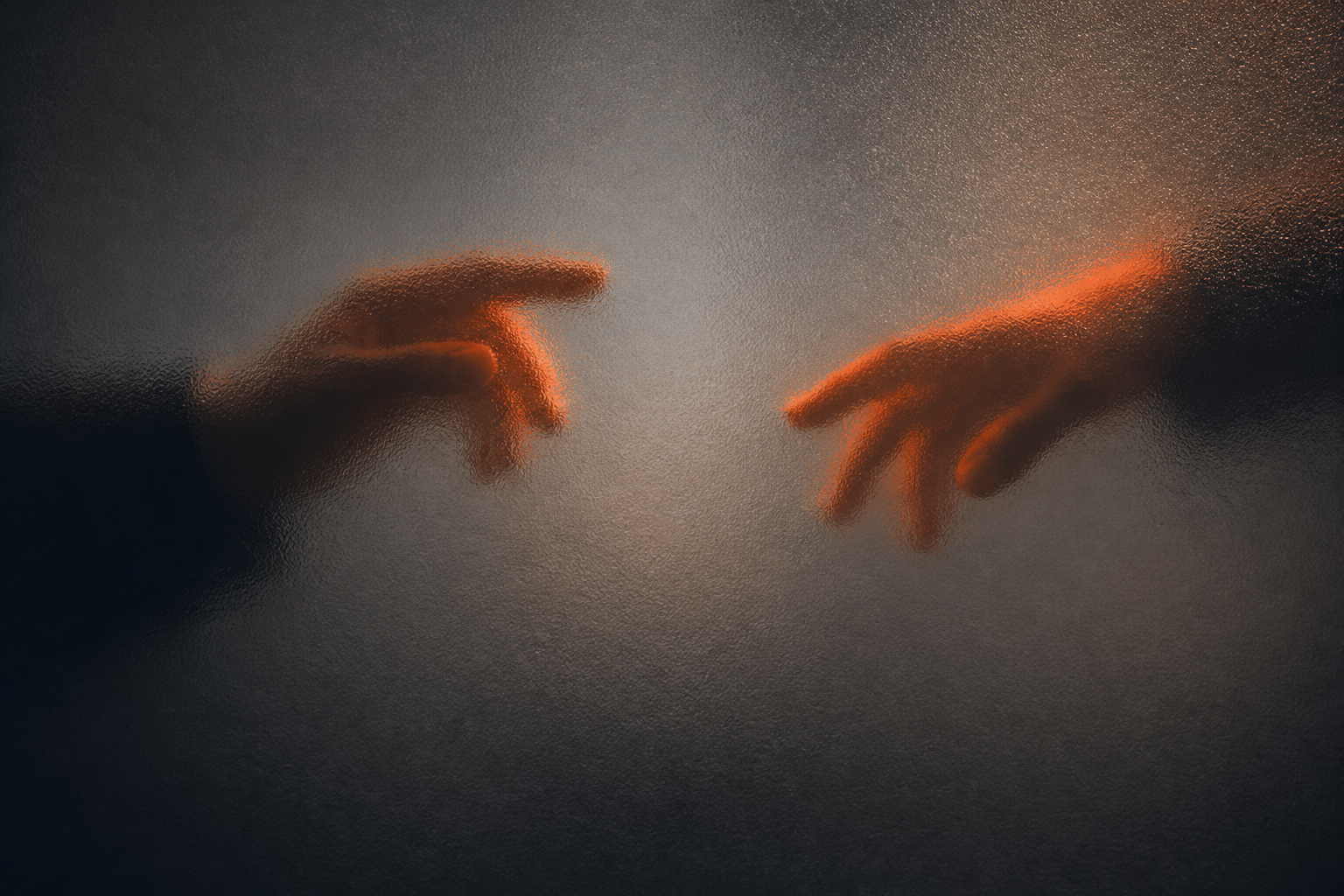 Dos manos desenfocadas acercándose detrás de vidrio esmerilado con luz naranja